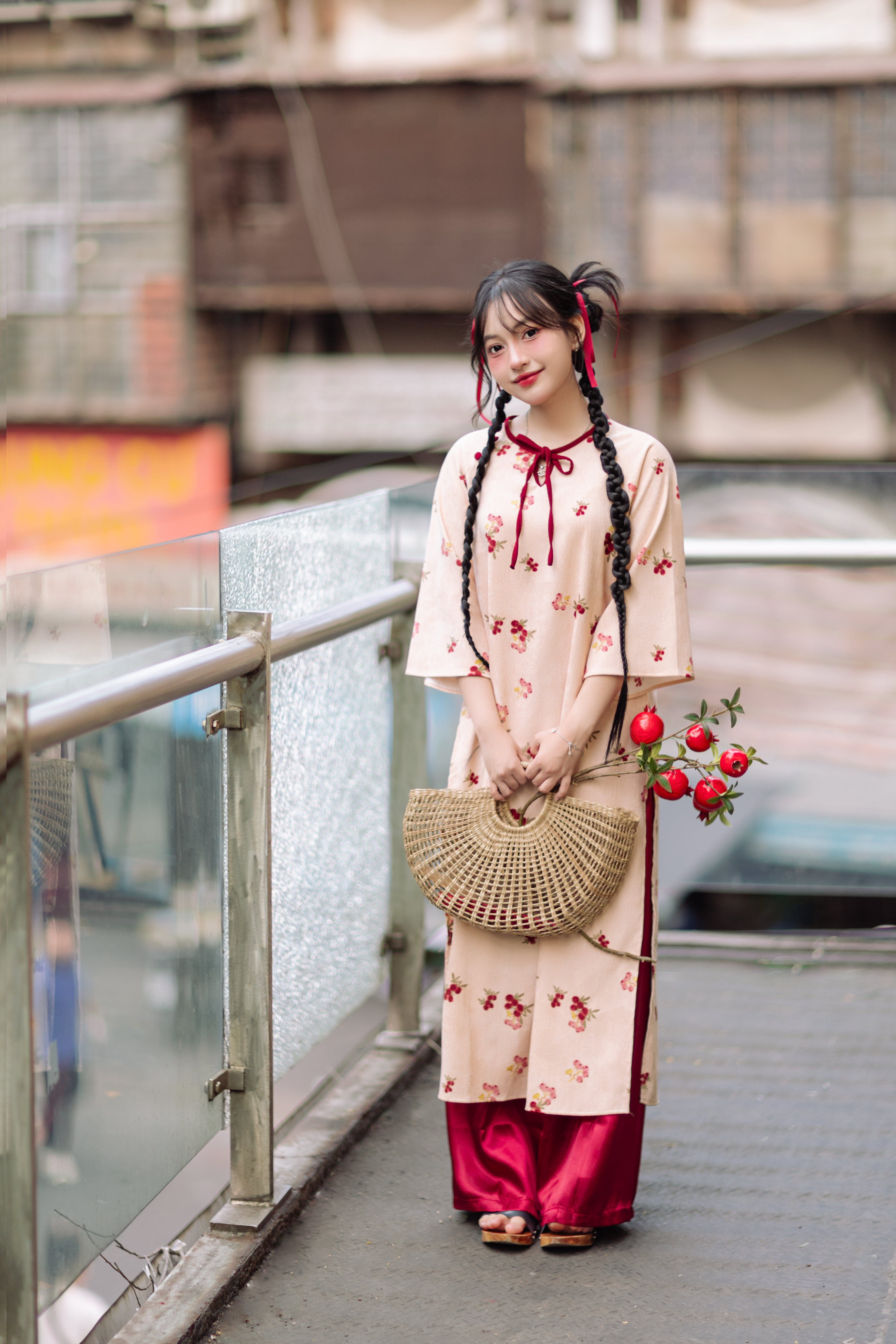 Young woman in floral attire with a woven bag and flowers standing outdoors on a sunny day.