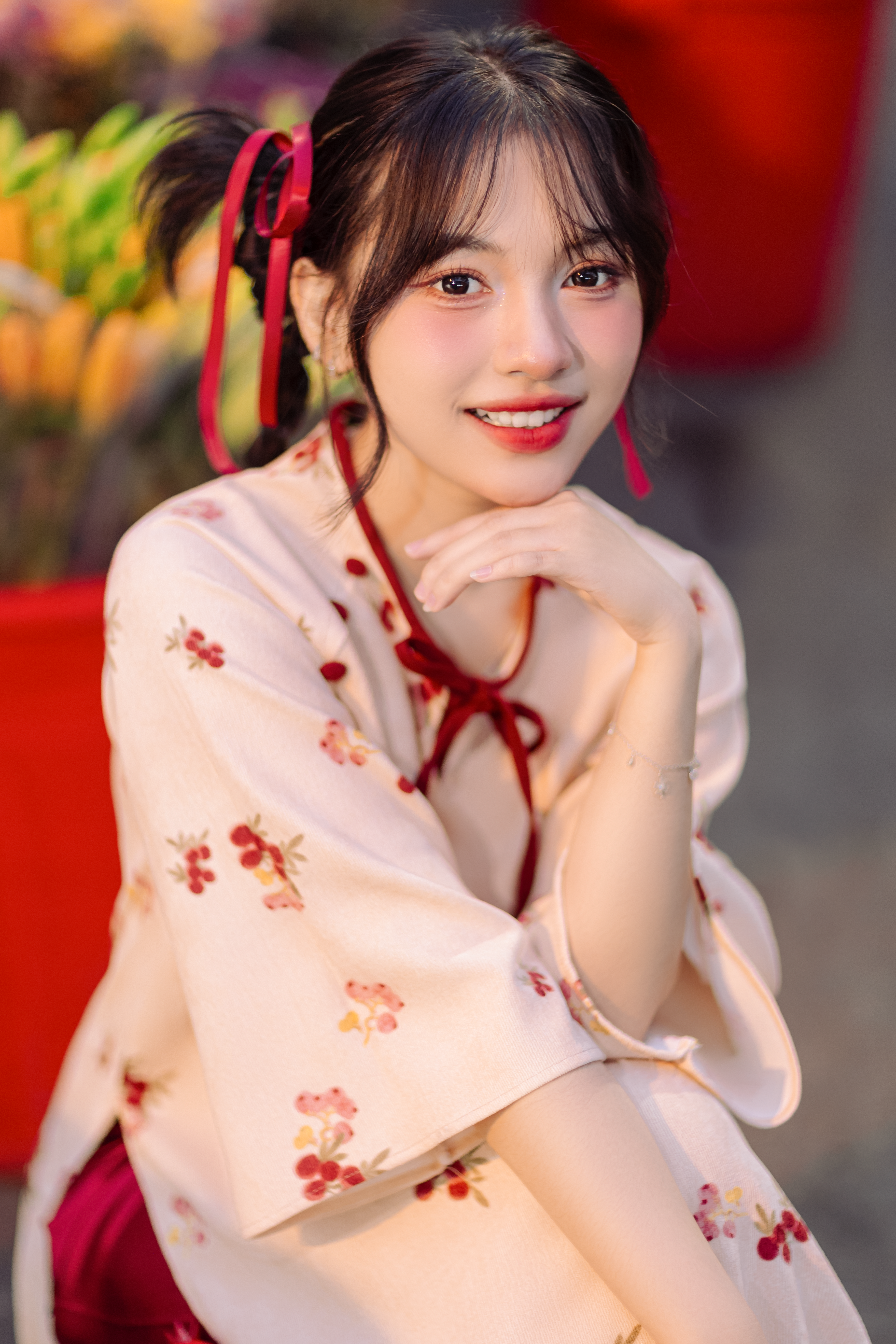 Charming woman in a floral kimono smiling warmly, outdoors with blurred floral background.