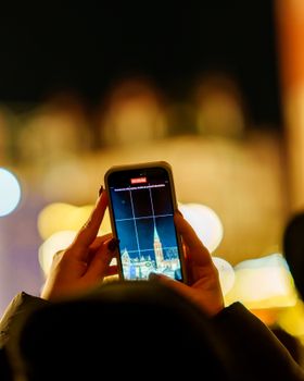 A person photographing a famous landmark with a smartphone at night.