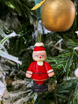 Close-up of a wooden Santa ornament hanging on a Christmas tree branch.