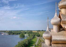 Wooden domes rise against a blue sky, overlooking a peaceful lake and lush greenery.