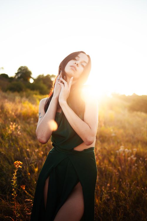 Free A woman in a green dress poses gracefully in a sunlit autumn field, capturing the warm essence of fall. Stock Photo
