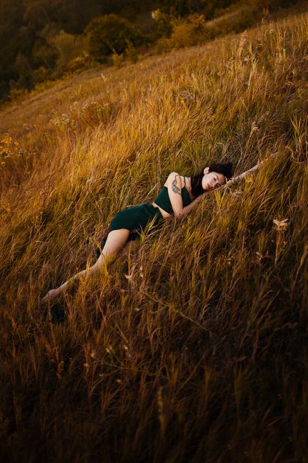 A woman with tattoos in a green dress relaxes in a field during an autumn sunset, capturing a serene fall vibe.