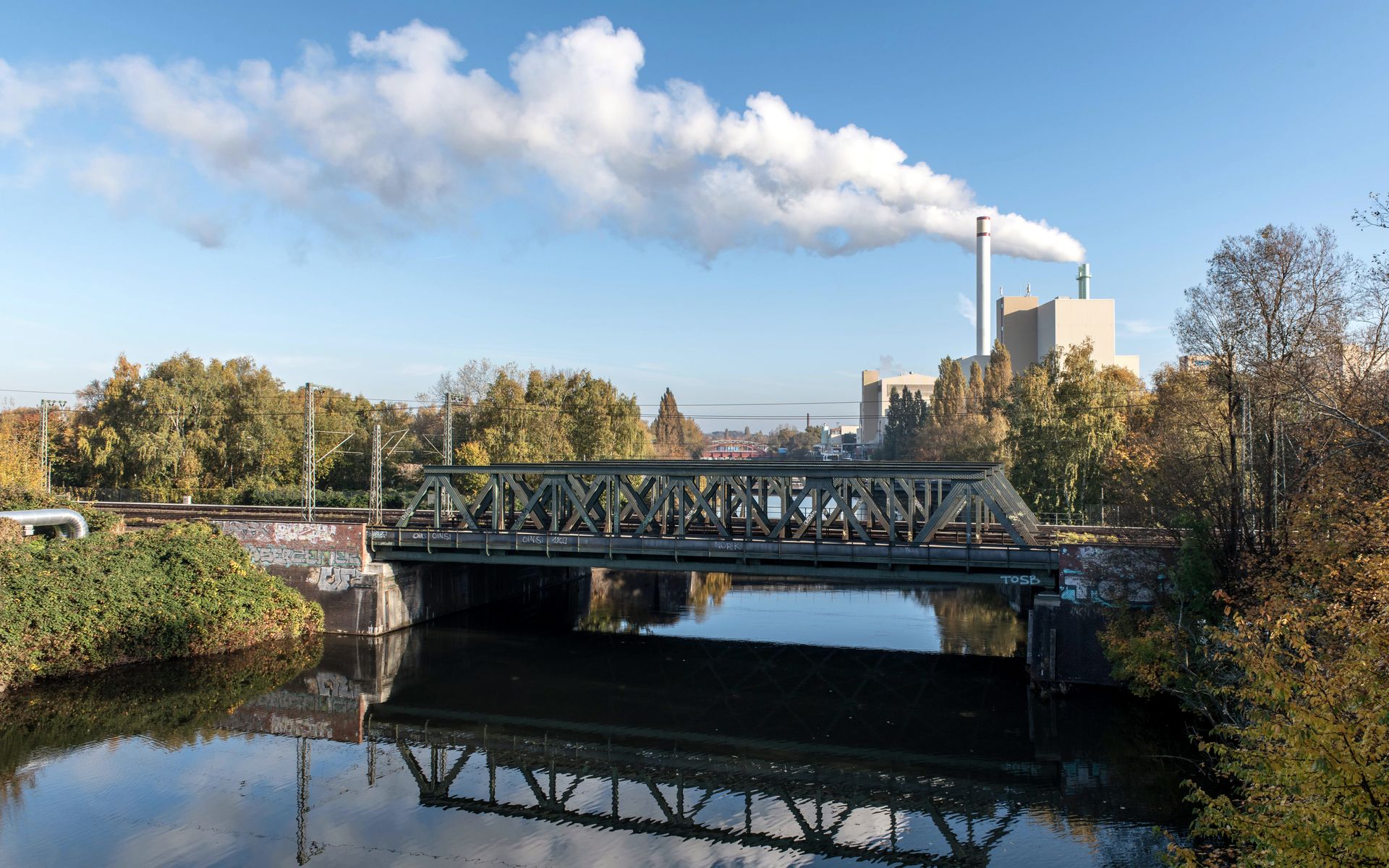 Scenic view of a railway bridge over a canal with an industrial facility in Hamburg.