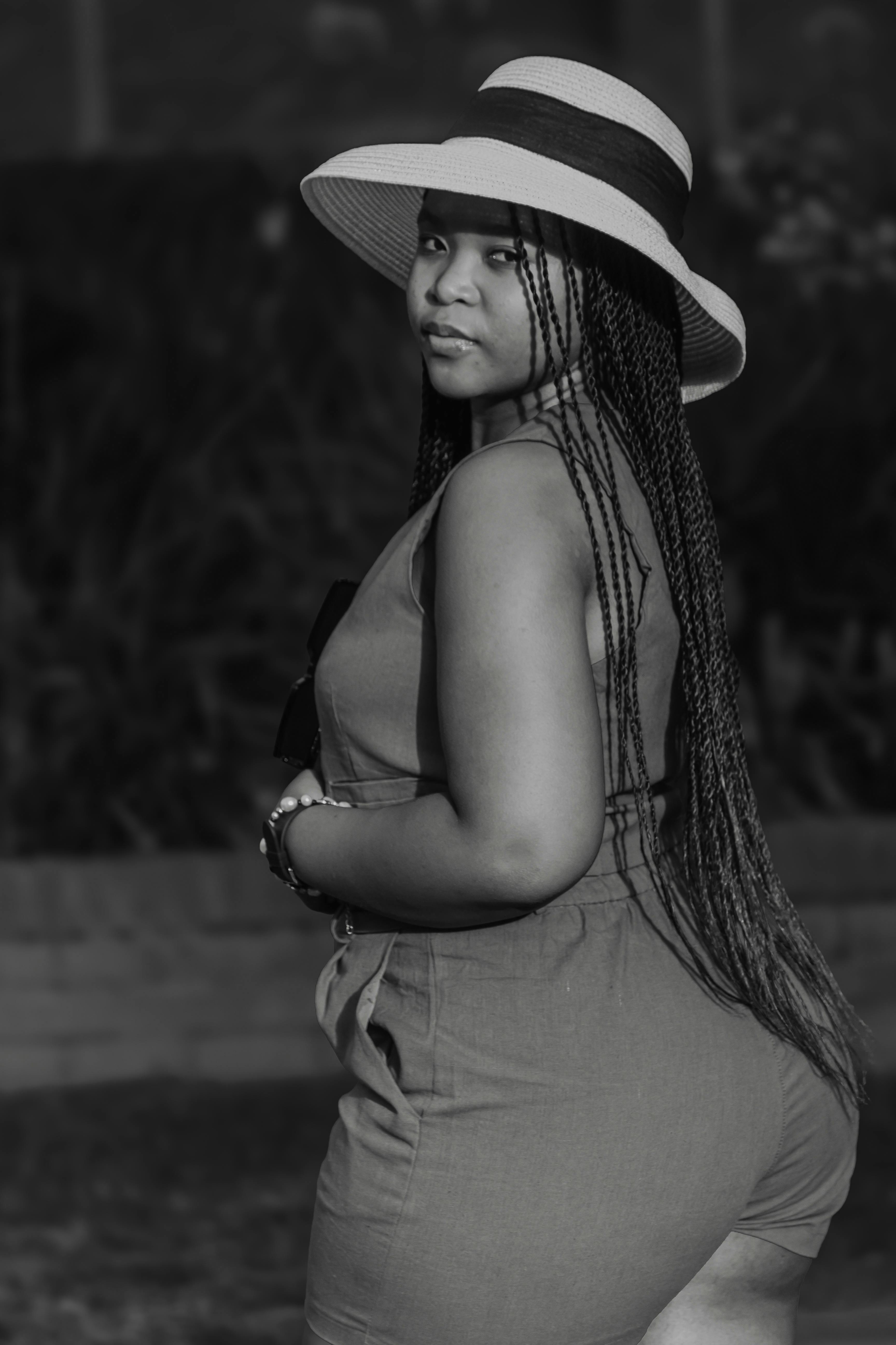 Black and white portrait of a young woman wearing a hat, showcasing confidence and elegance outdoors.