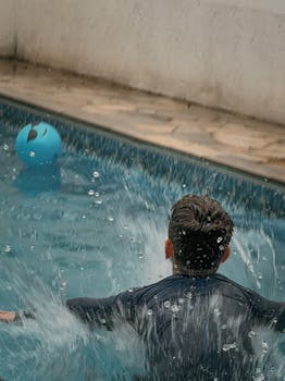 Man making a splash while entering a swimming pool.