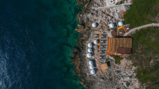 Stunning aerial view of a rocky coastline resort with white umbrellas by the clear blue sea.