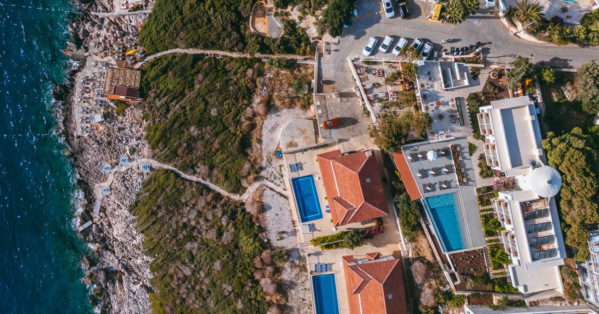 Aerial view of coastal villas with swimming pools and rocky shoreline