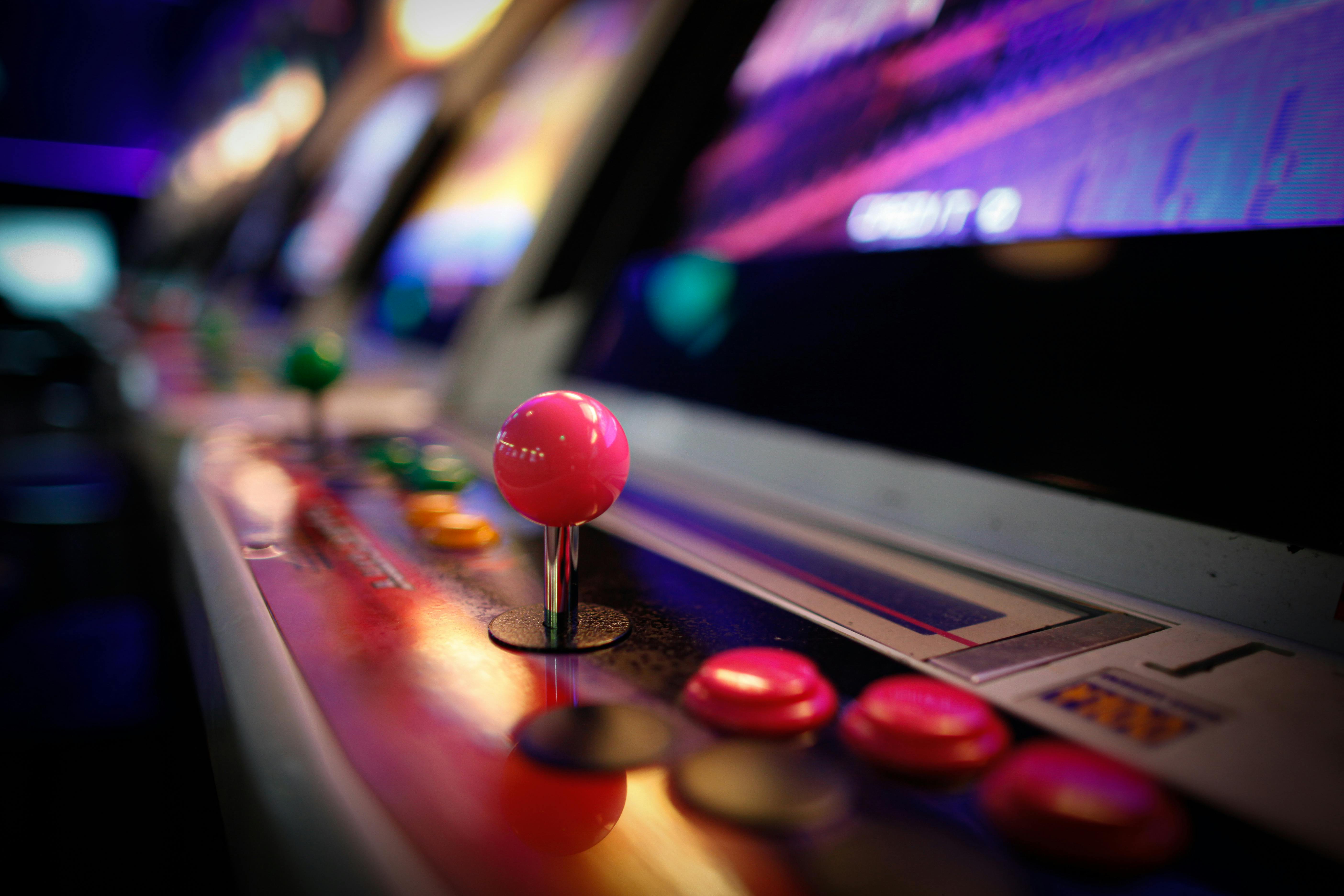 Close-up of a colorful vintage arcade machine with glowing joysticks and buttons in a dimly lit game room.