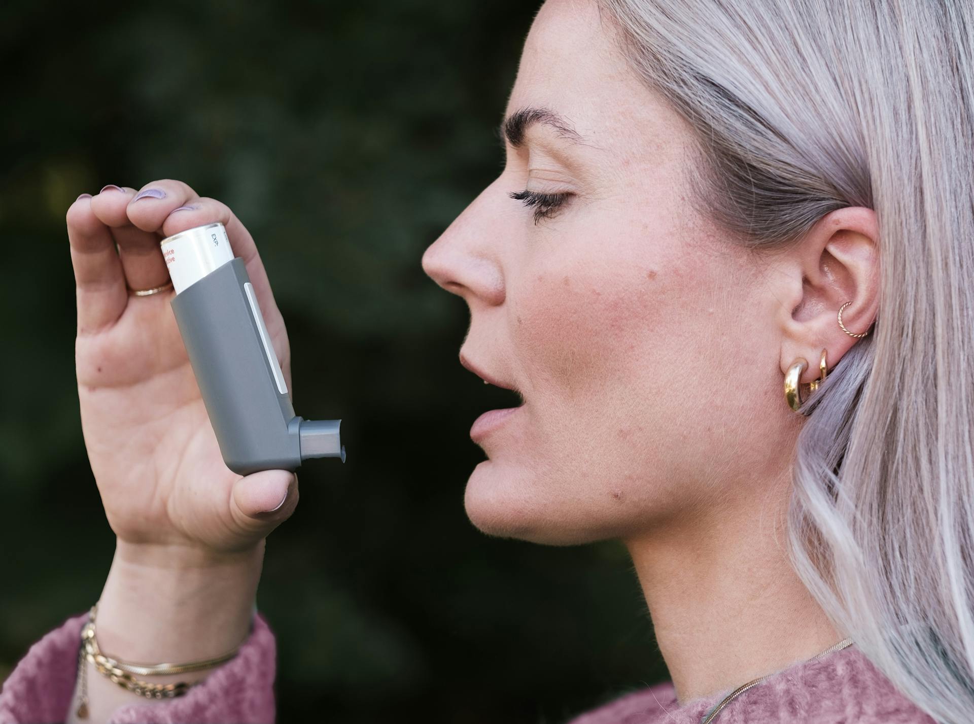 Close-up profile shot of a woman using an asthma inhaler outdoors, highlighting healthcare essentials.