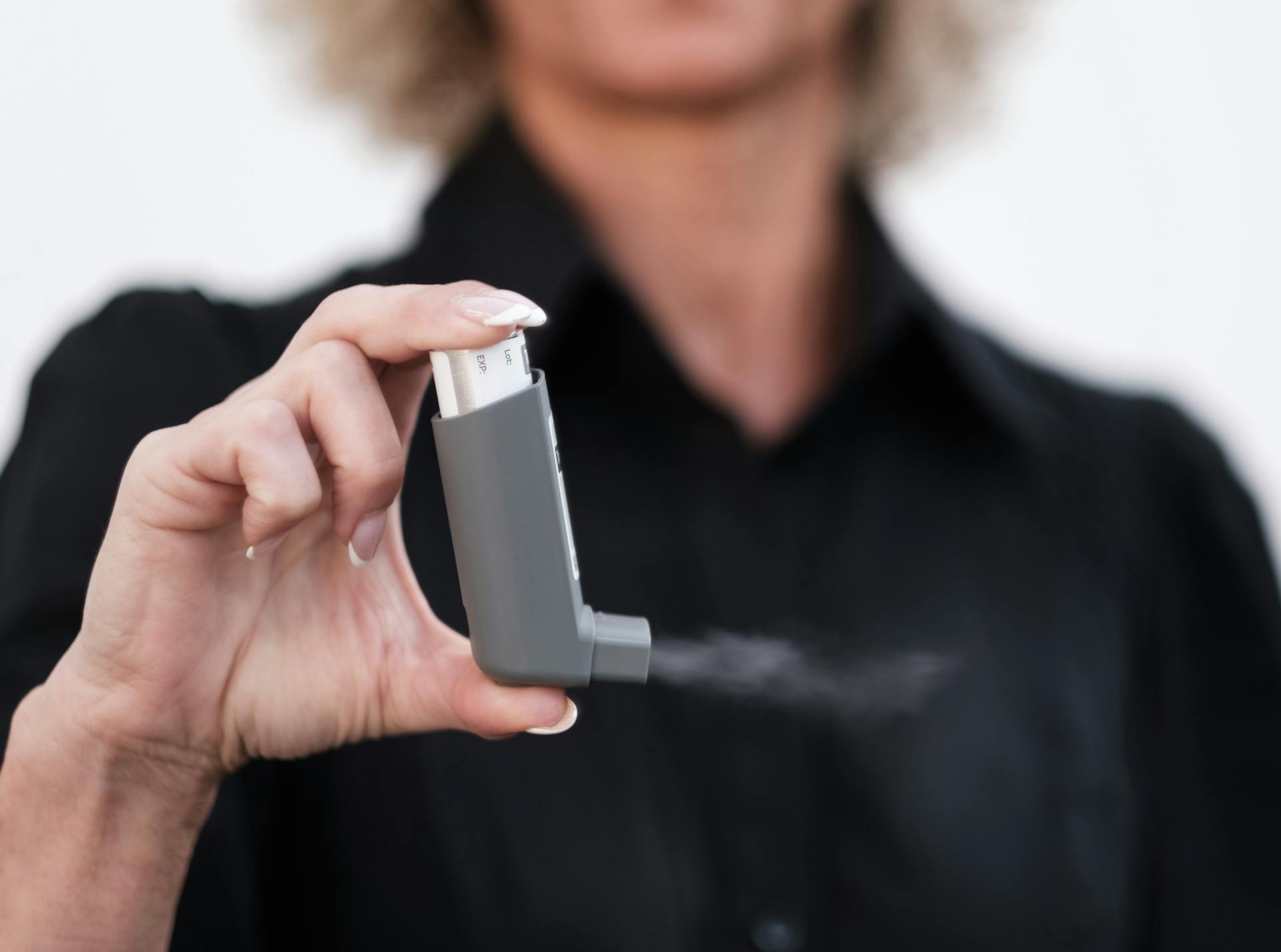 Person holding and using an inhaler, showcasing healthcare and respiratory care indoors.