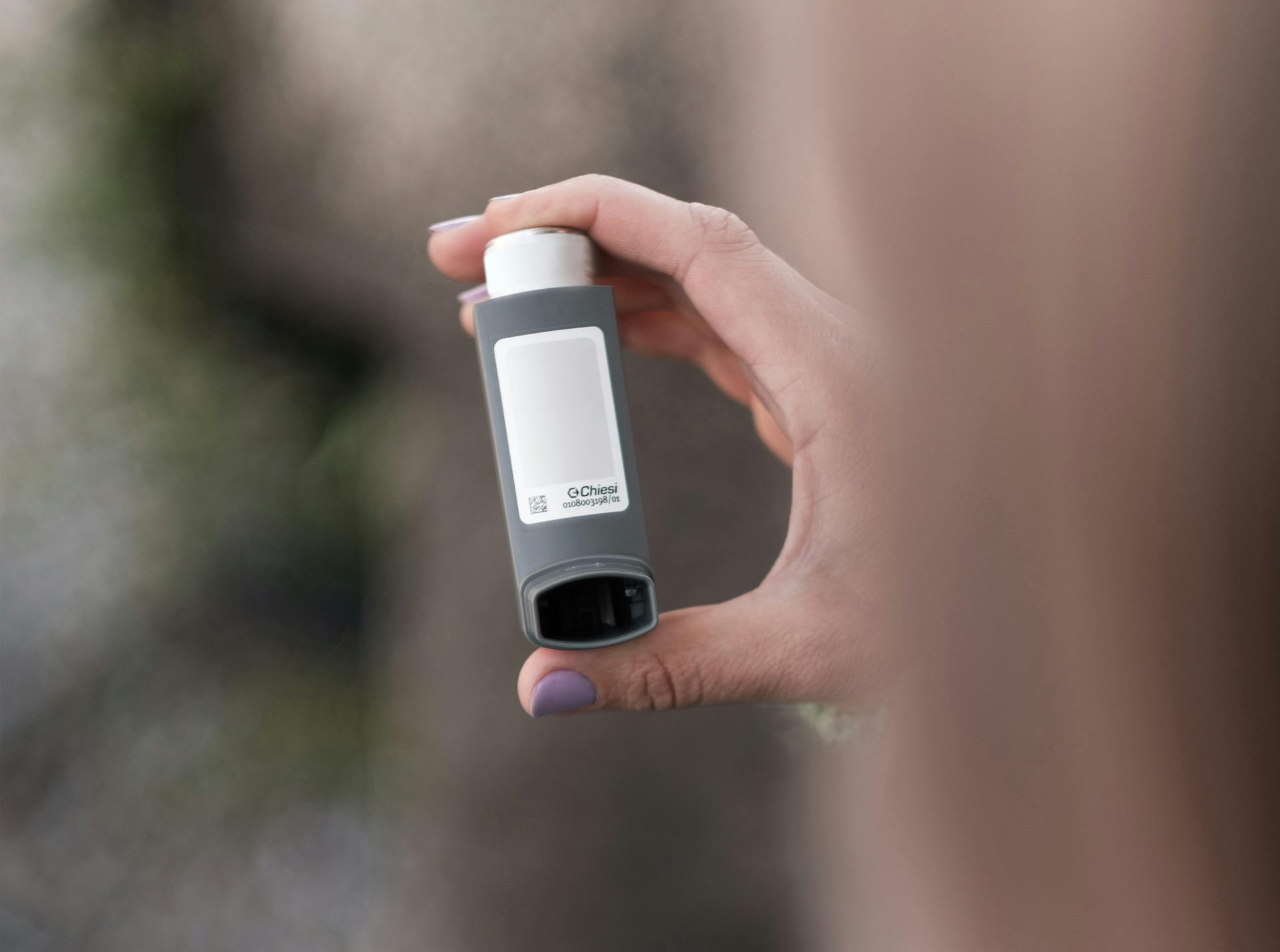 A person holding a gray asthma inhaler outdoors. Health and medical concept.