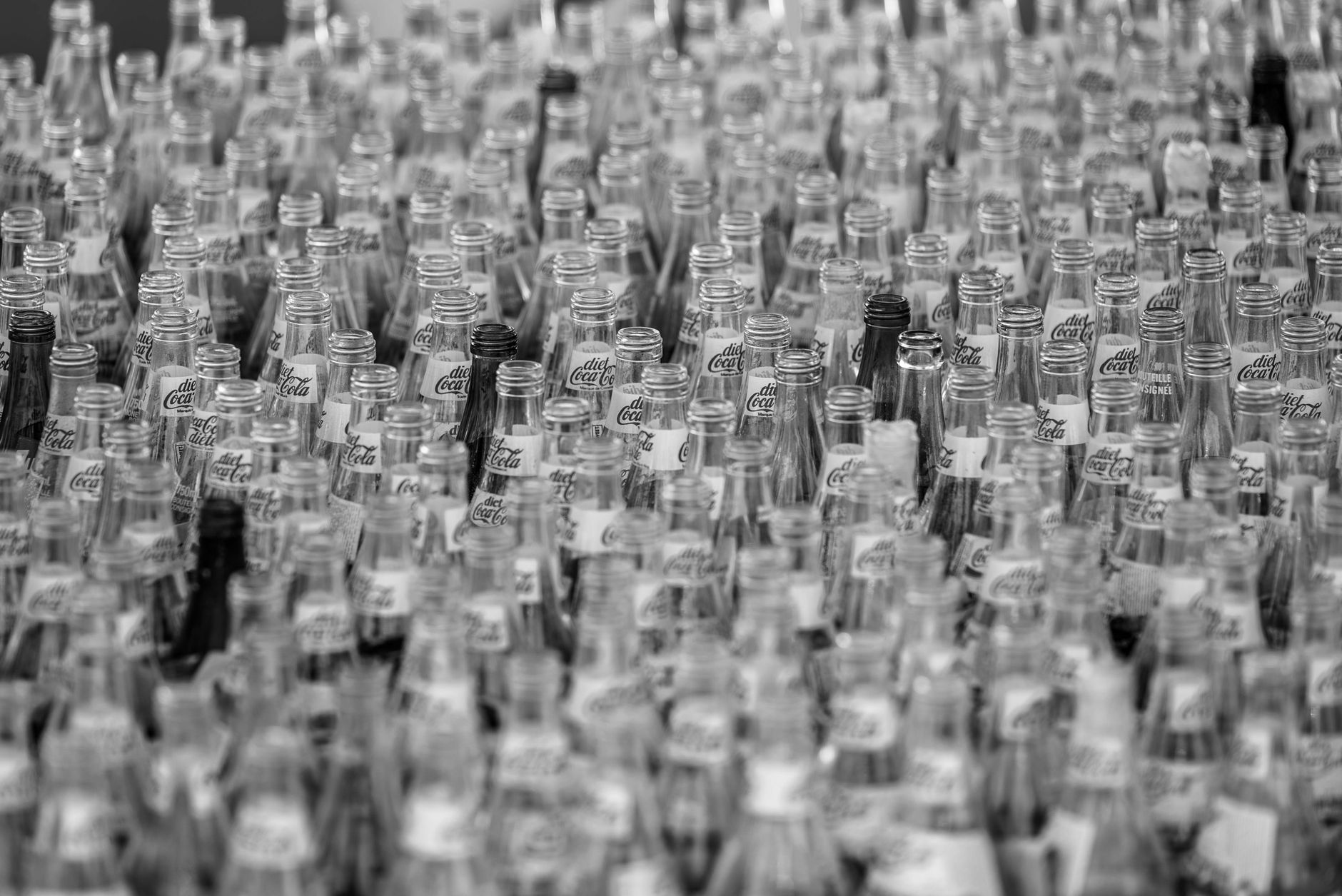 A monochrome image showcasing numerous empty Coca-Cola glass bottles with selective focus.