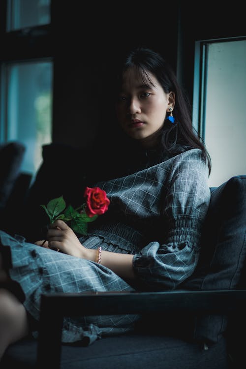 女人穿著灰色的衣服，坐在沙發上抱著紅玫瑰