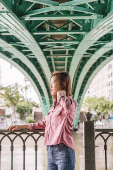 阳光明媚的日子里，一位时尚女士在绿色的城市桥下摆姿势，展现时尚与优雅