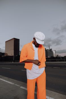Stylish individual in vibrant orange attire stands confidently urban setting.