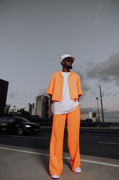 Stylish urban fashion model in a bright orange outfit standing on a city street.