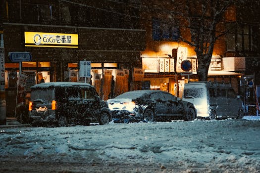 Snow-covered cars outside a lit Tokyo restaurant at night, capturing winter's beauty.