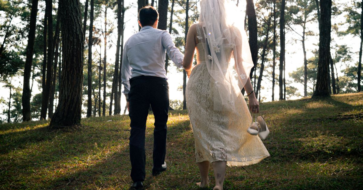 Bride and groom walking in a sunlit forest in Hà Giang, Vietnam.