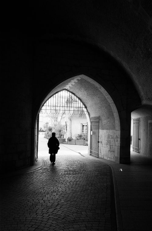Free Black and white photo of a silhouette walking through an ancient archway in Nancy, France. Stock Photo