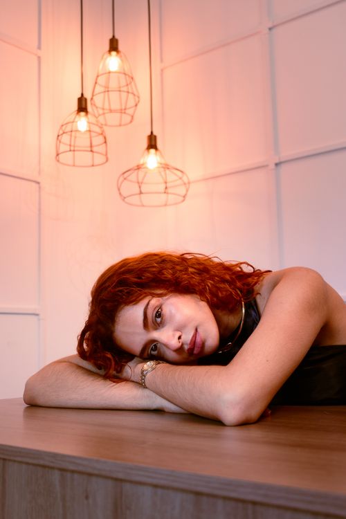 Free Portrait of a serene woman with red hair resting on a table indoors, Brazil. Stock Photo