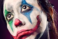 一张小丑的特写肖像，脸上涂着色彩缤纷的油彩，眼睛富有表情，妆容充满戏剧性