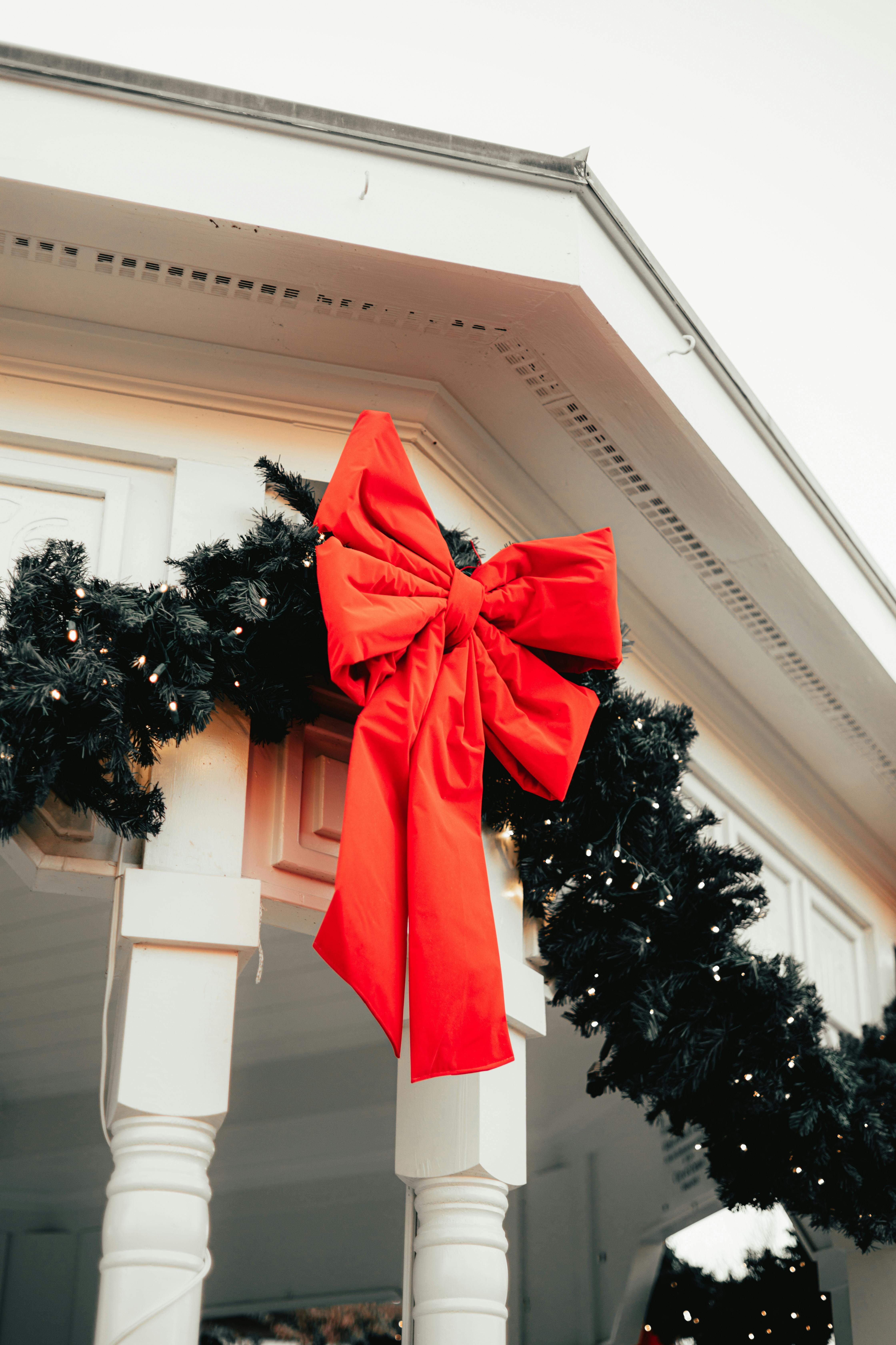 A close-up of a holiday garland with a bright red bow on a building corner.