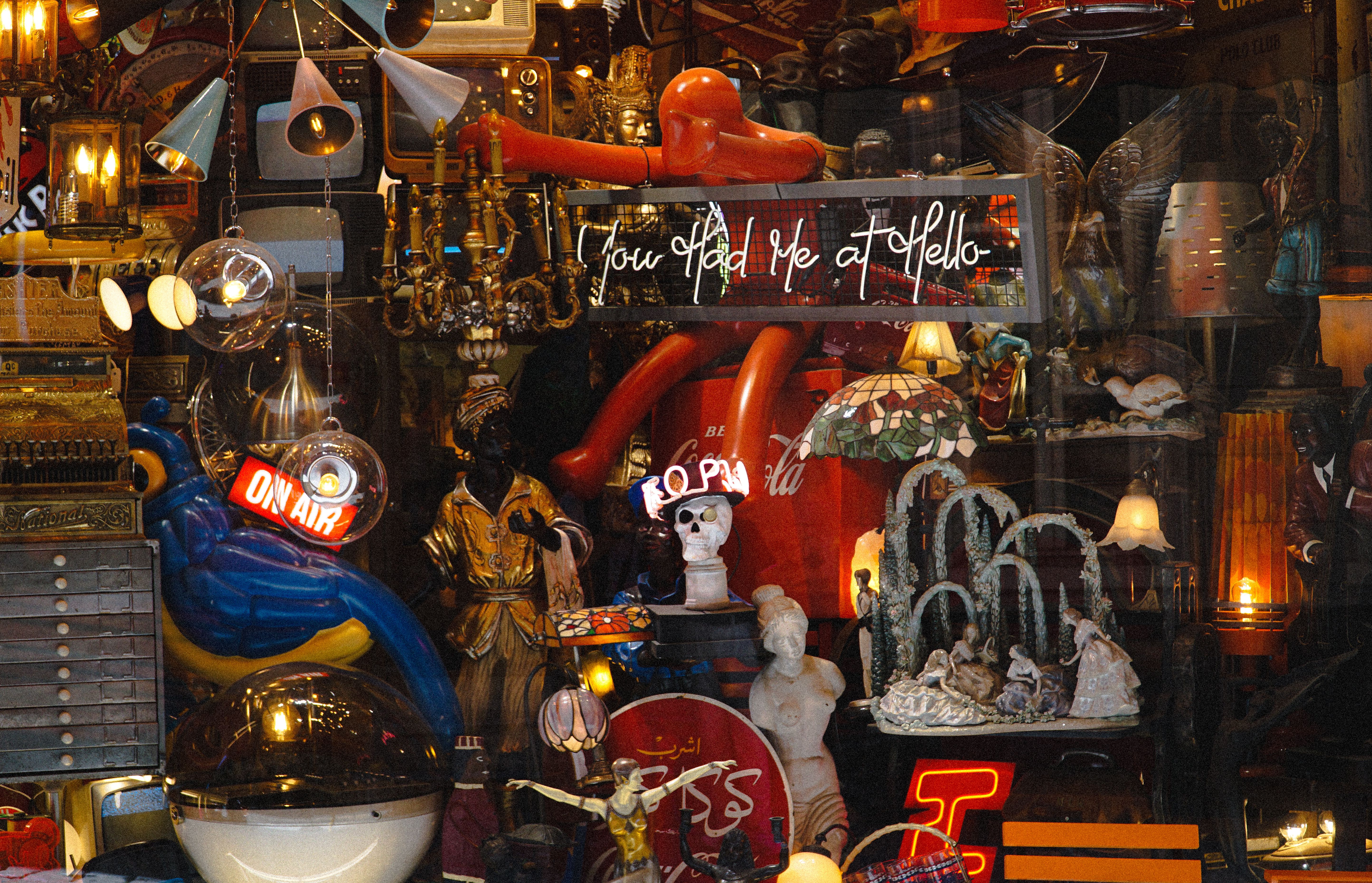An eclectic display of antiques in a shop window featuring neon signs and retro decor.