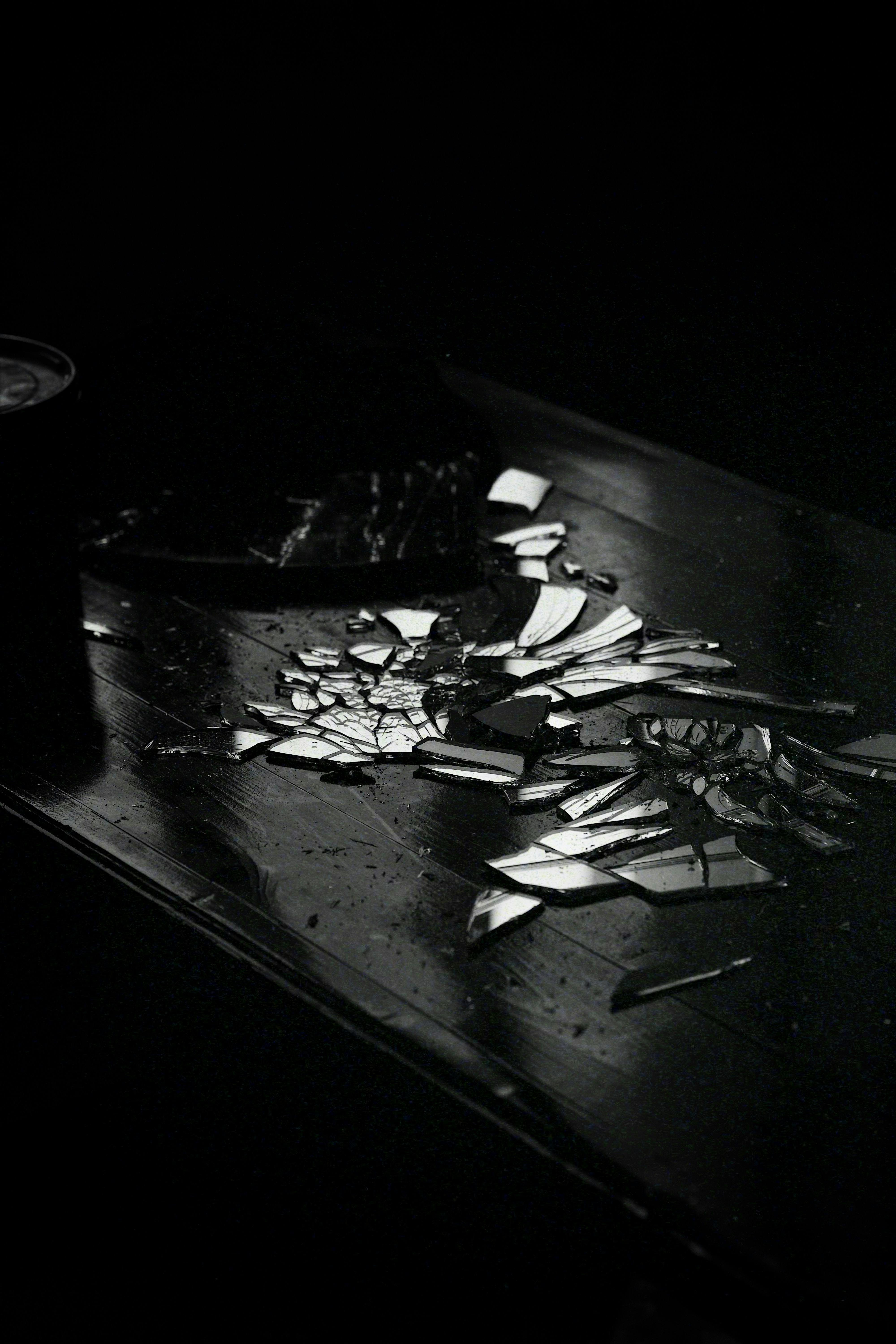 grátis Uma foto dramática em preto e branco de vidro quebrado em uma superfície reflexiva com tons escuros. Foto profissional