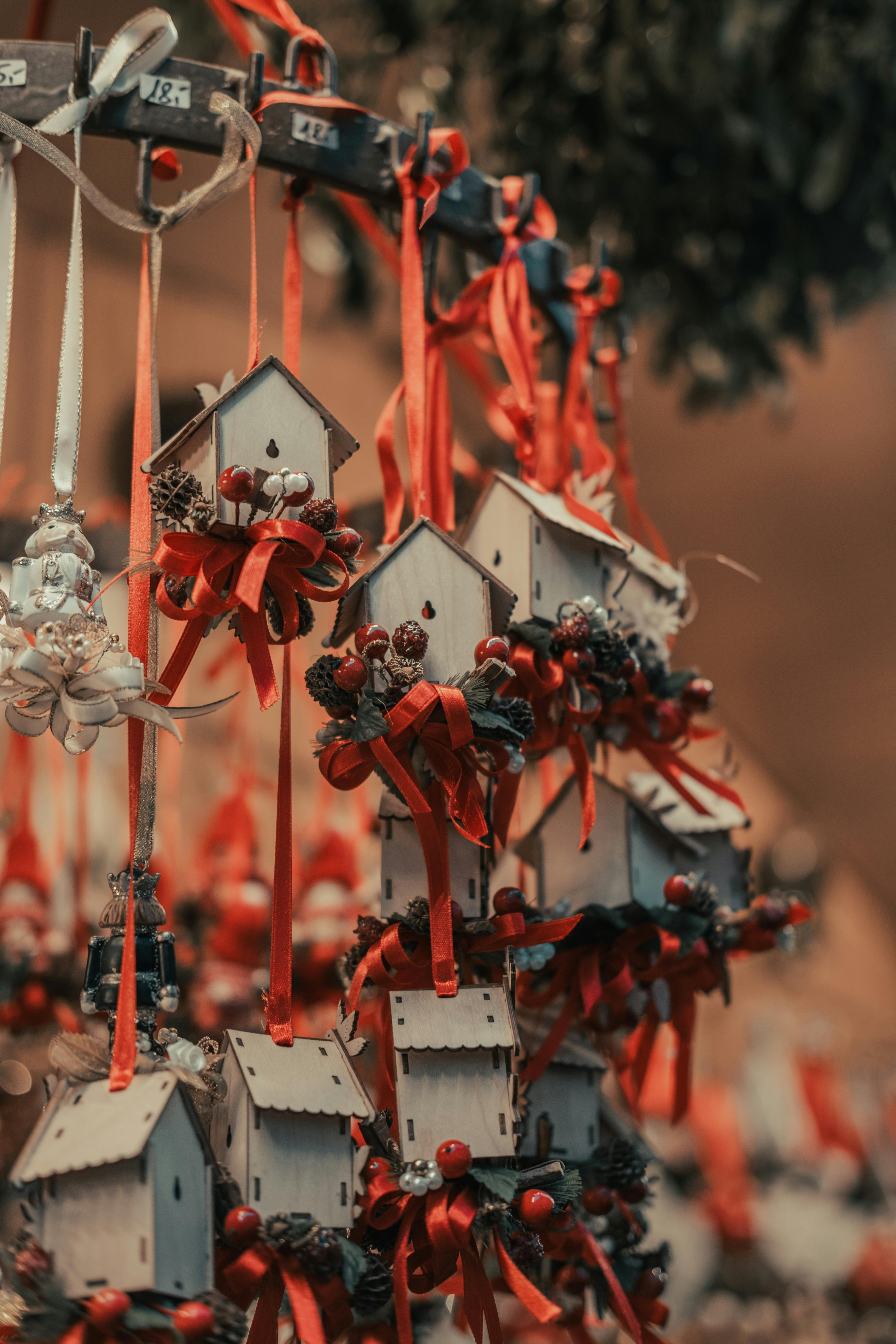 A close-up of wooden birdhouse Christmas ornaments adorned with red ribbons, berries, and pine cones.