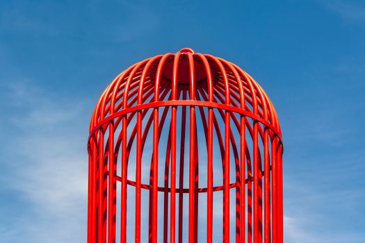 Colorful red birdcage reaching towards the bright blue sky, symbolizing freedom.