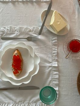 Stylish table setting with bread and red caviar, butter, and crystal glass in daylight.