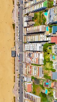 Aerial shot of a coastal city street lined with homes and beach access, showcasing urban and natural blend.
