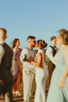 Bride and groom share a romantic dance surrounded by guests at sunset.