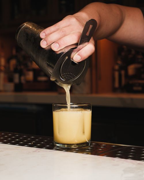 Free Close-up of a bartender pouring a freshly shaken cocktail into a glass at a bar counter. Stock Photo