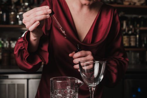 Free A bartender in a red dress adding bitters to a cocktail in a bar setting. Stock Photo