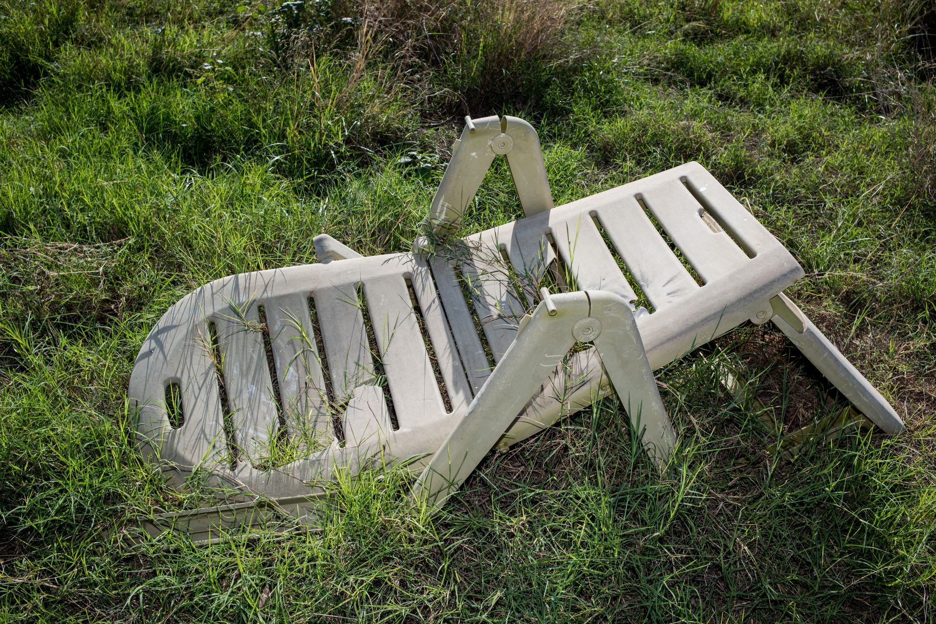 An old, broken plastic lawn chair lying in overgrown grass outdoors.