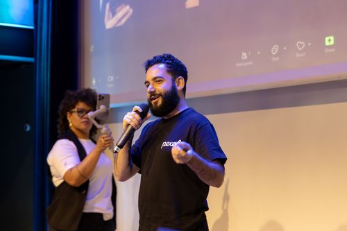 Free Man presenting with microphone while woman records with phone on stage. Stock Photo