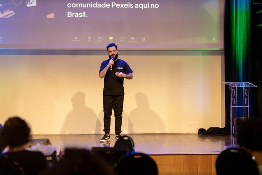 Man speaking on stage with a microphone at a conference in Brazil.