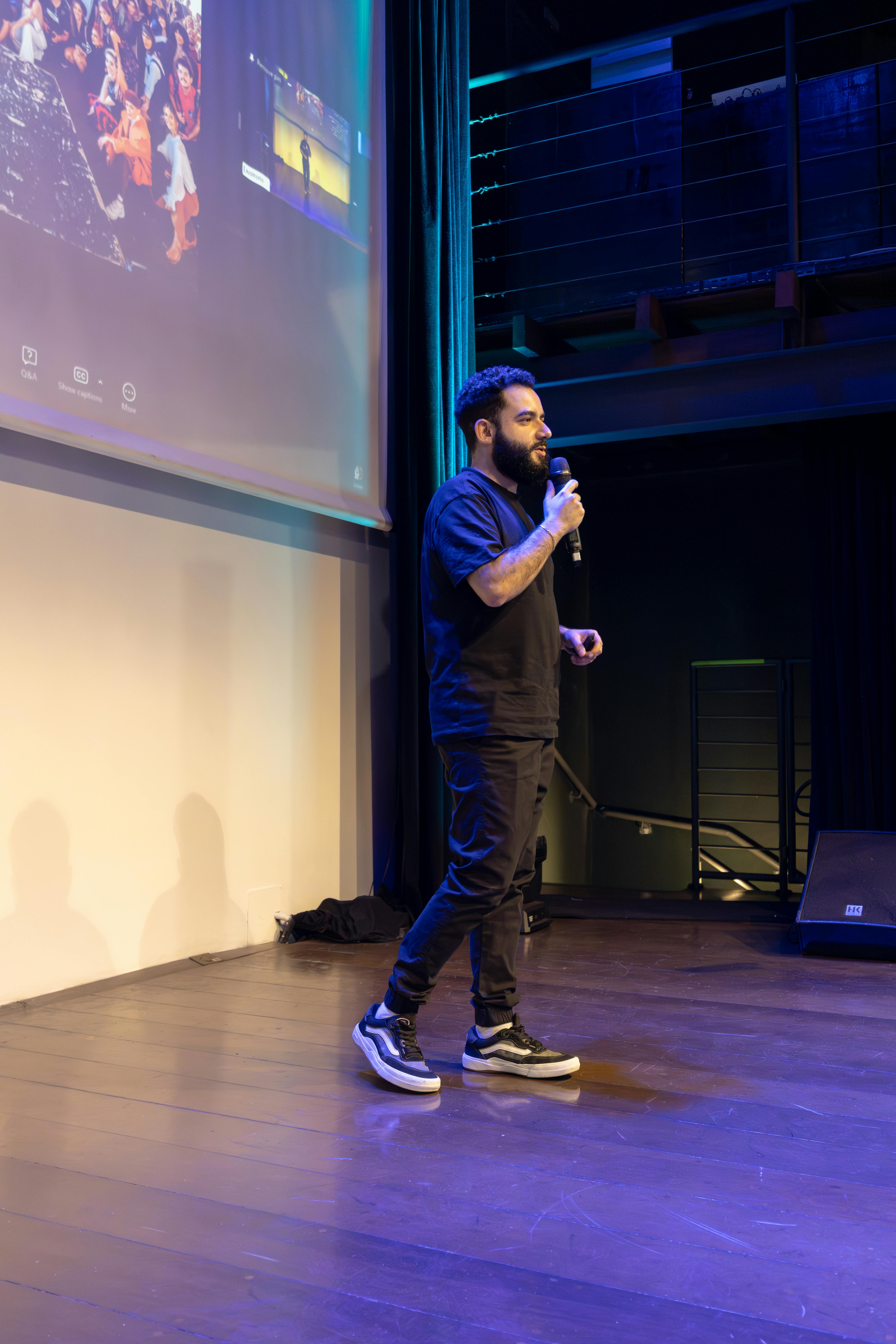 Ücretsiz Bir konferans sırasında iyi aydınlatılmış bir sahnede mikrofonla konuşma yapan bir adam. Stok Fotoğraflar