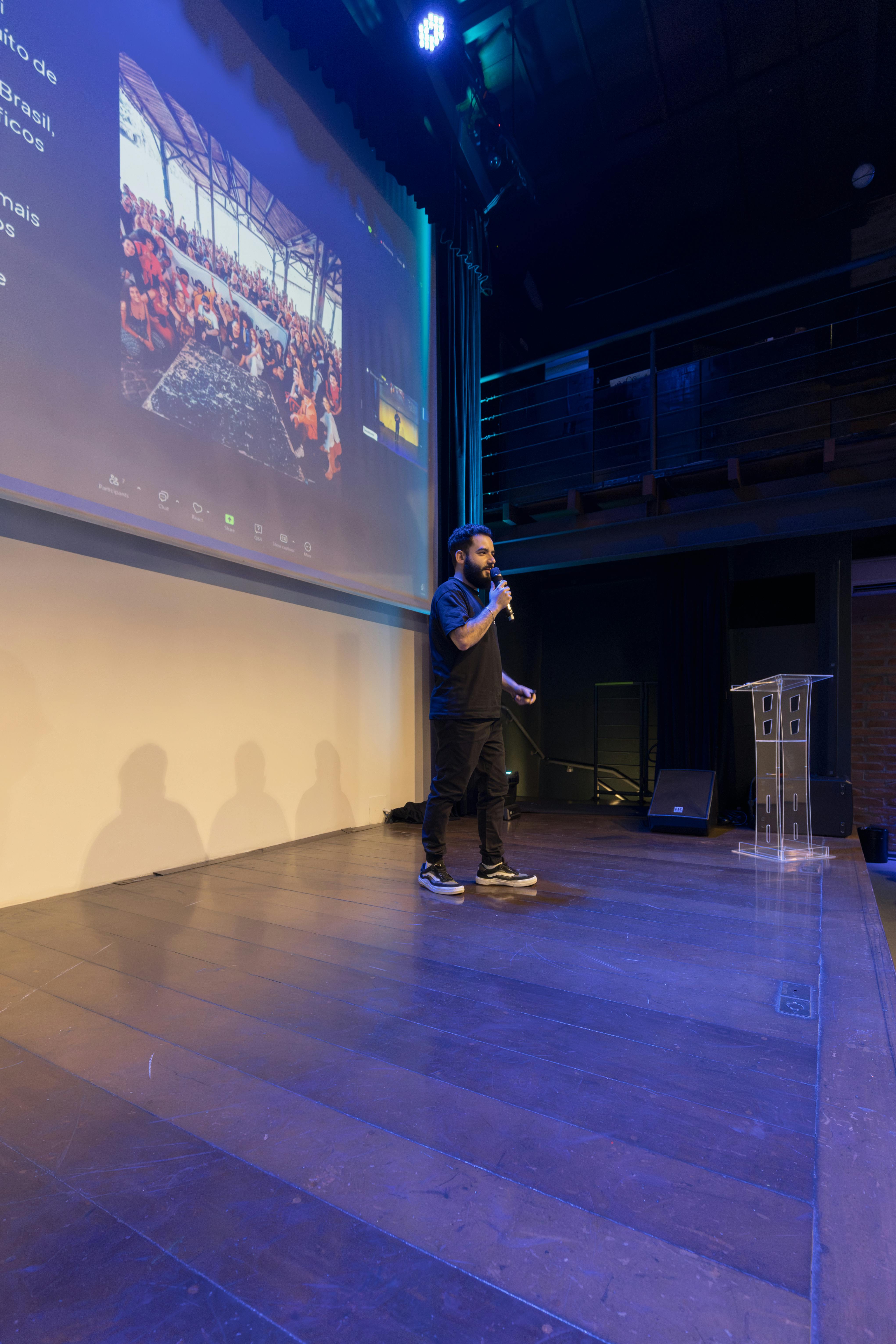 Hombre dando una presentación en el escenario con una pantalla digital en un lugar moderno.