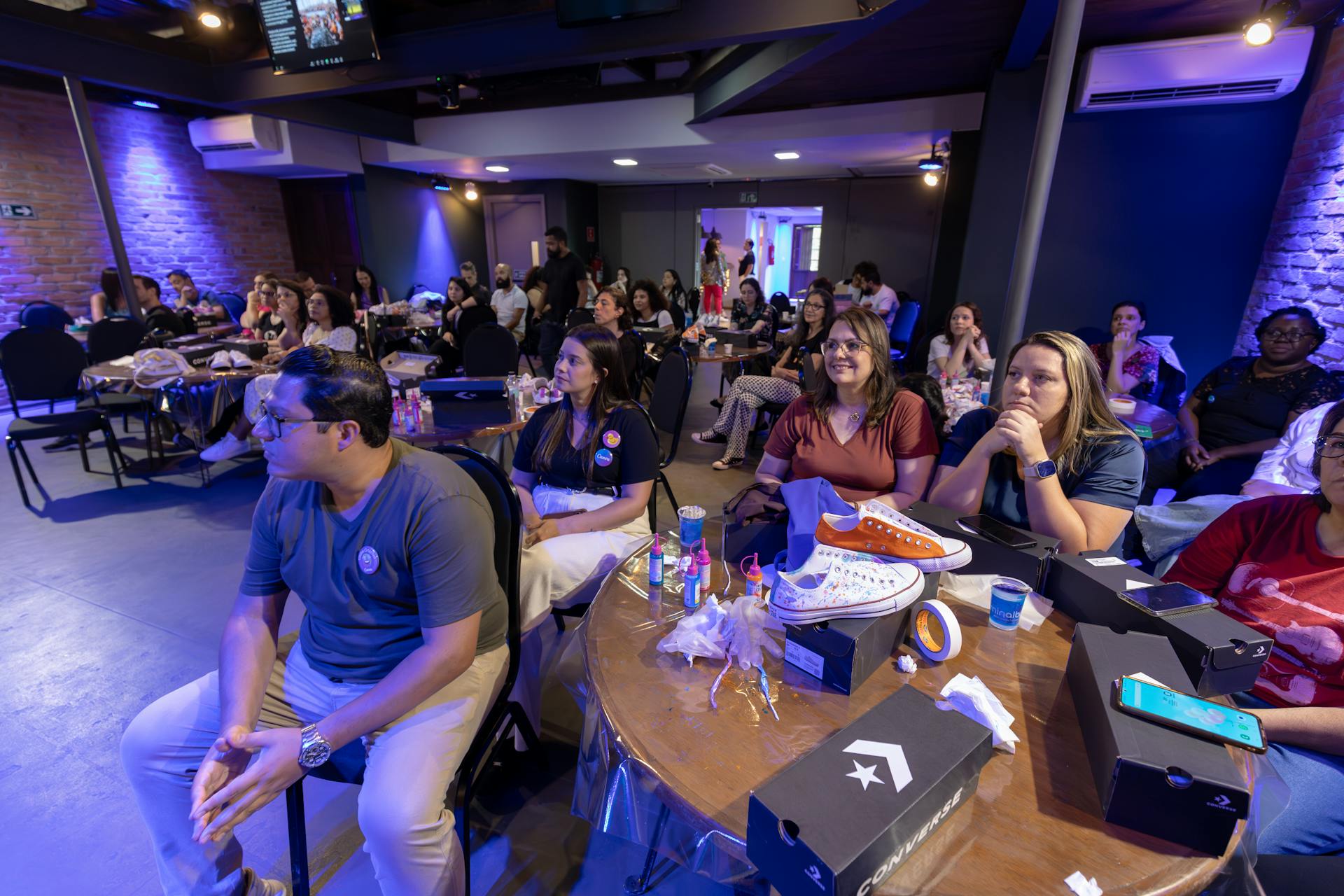 Group of adults attending an indoor workshop featuring Converse sneakers on table.