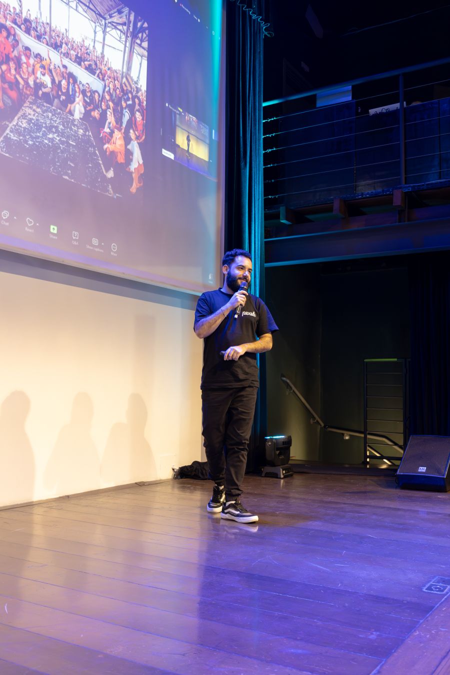 A presenter on stage with an audience image on screen