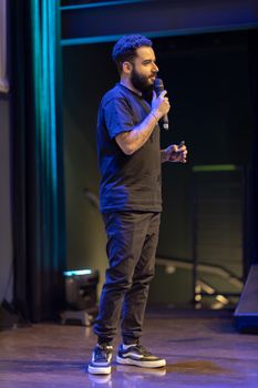 A man speaks into a microphone on stage during an indoor event.