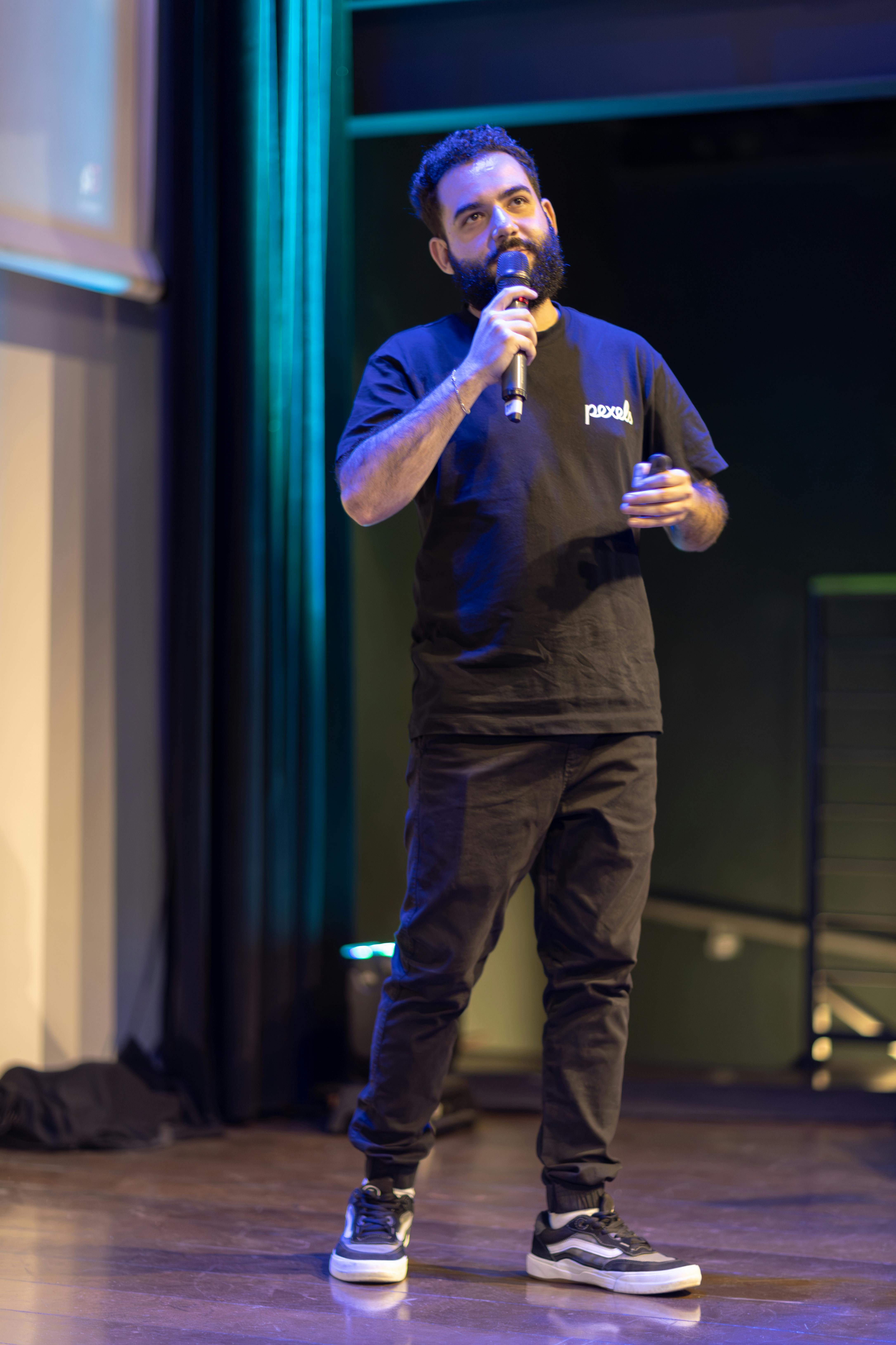 Man speaking on stage with microphone at an indoor conference event.