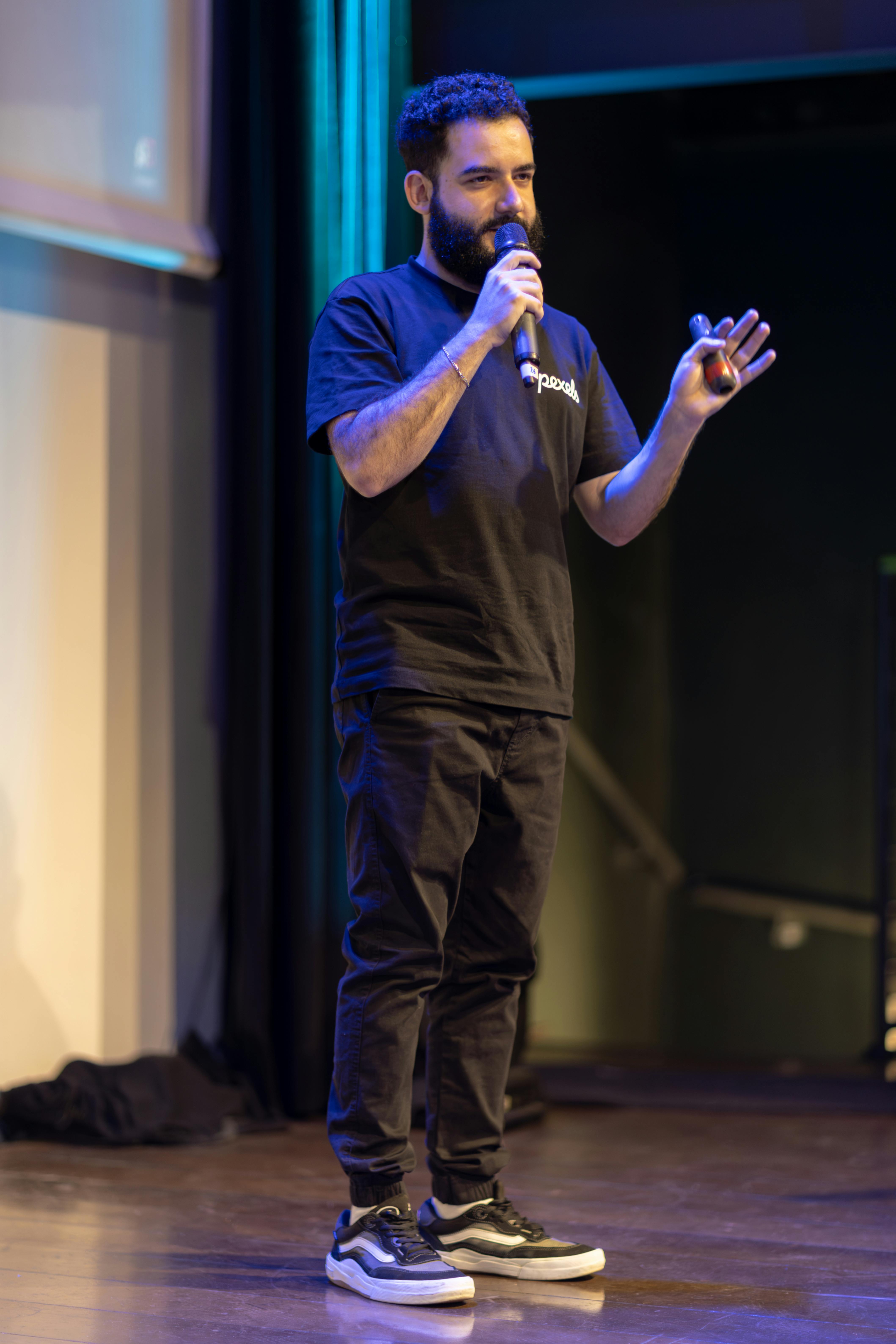 Man speaking on stage with microphone, engaging audience.