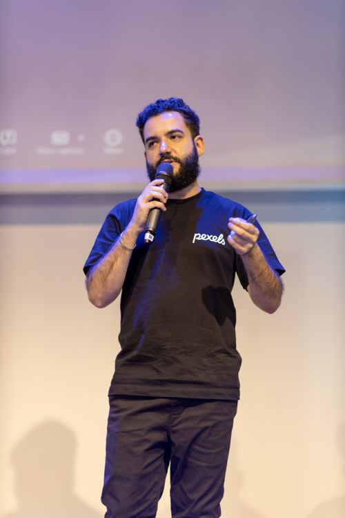 Free A confident speaker presenting with a microphone on stage under professional lighting. Stock Photo