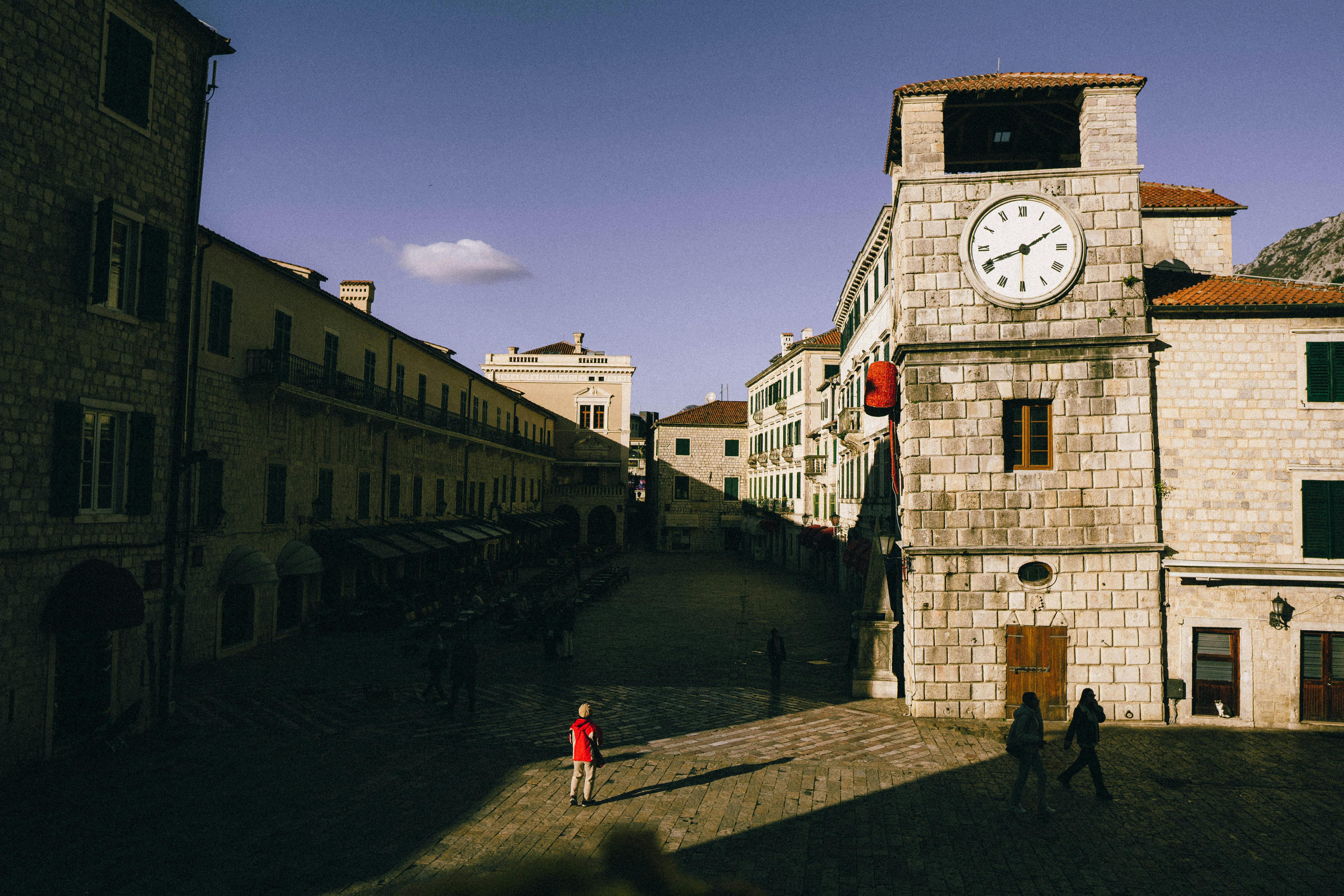Sunlit clock tower and medieval architecture at Kotor's Old Town square.