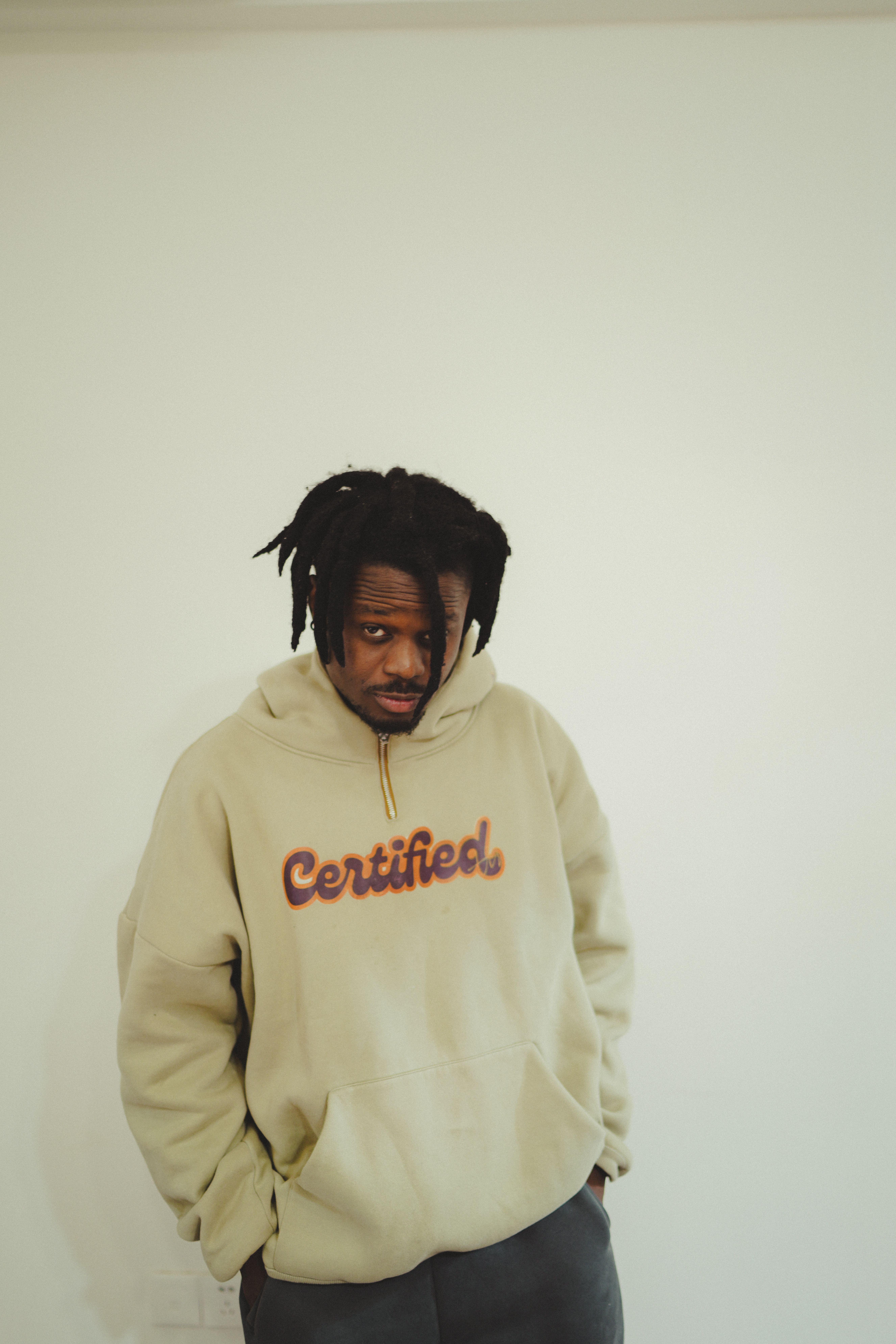 Young man wearing a beige hoodie against a minimalistic indoor background.