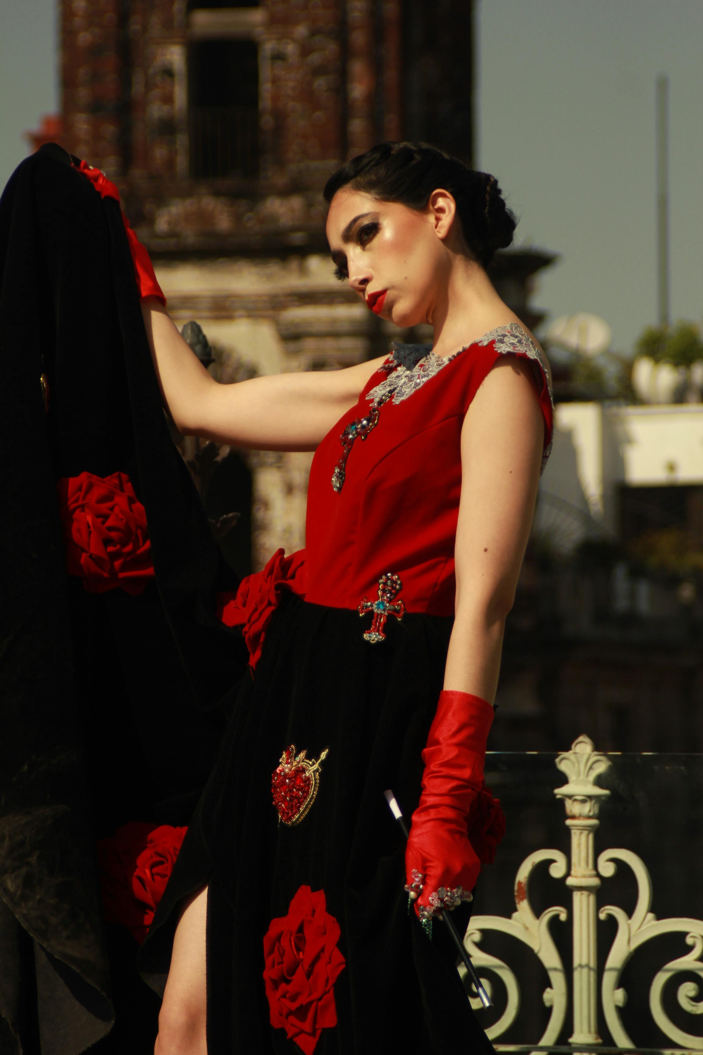 Stylish woman in red dress posing elegantly outdoors with a historic urban setting.